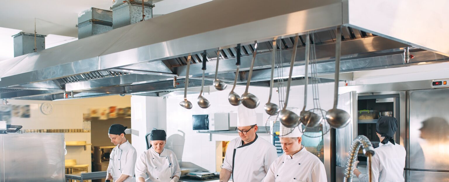 Five chefs wearing uniforms posing in a kitchen
